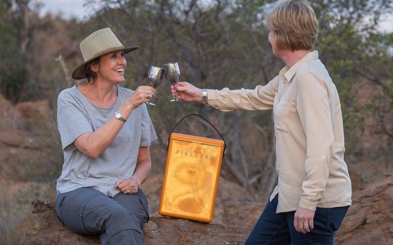 Two women enjoying a sunset toast during a safari sundowner in the African bush—part of a daily safari tradition led by Marula Hill Travel.