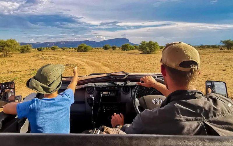 A child joins a safari guide on a game drive in South Africa, pointing towards the wild. Is South Africa safe for kids? With expert-led safaris, families can explore safely.