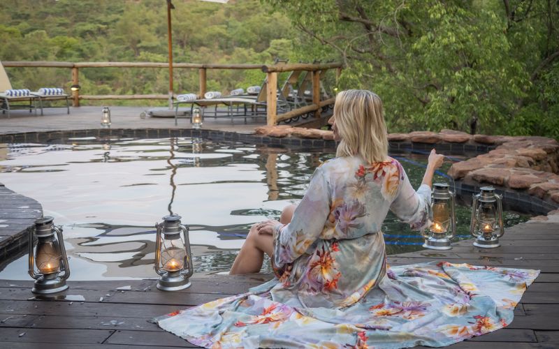 A guest relaxes by a lantern-lit pool at a luxury lodge in Welgevonden Game Reserve, a top choice for where to go on a malaria-free safari.