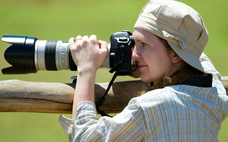 A photographer on a photographic safari, capturing wildlife through a professional camera with a telephoto lens, ready for the perfect shot.