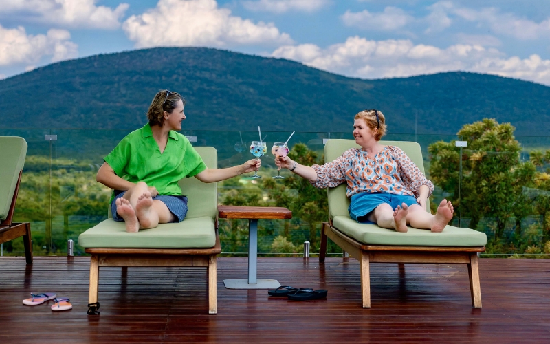 Sian Loehrer and Vikki Jackson enjoying sundowners on the deck at Babohi Safari Lodge in Qwabi Private Game Reserve, with views over the African bush.